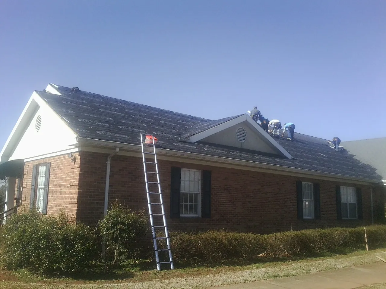 Crew tearing shingles off a brick ranch roof with a ladder set — Metal Roof Repair work by our crew in Linden